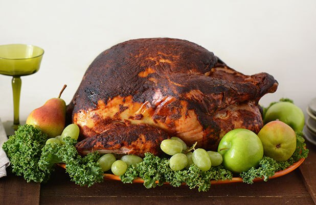 Un pavo entero con salsa de ancho sobre un lecho de verduras, uvas, y manzanas y peras enteras.